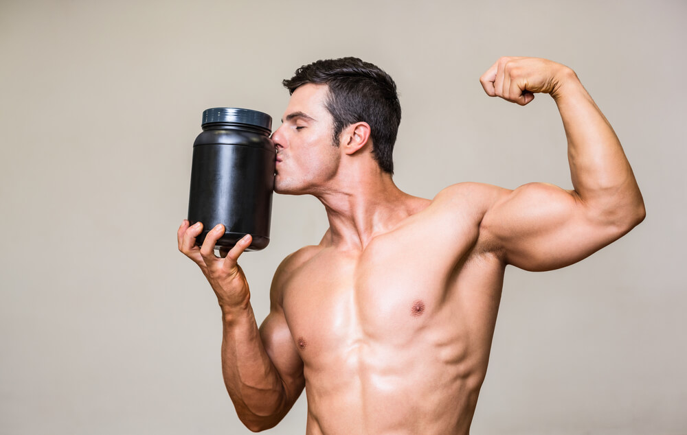 Muž so zatnutými svalmi pózuje s čiernou dózou proteínového prášku